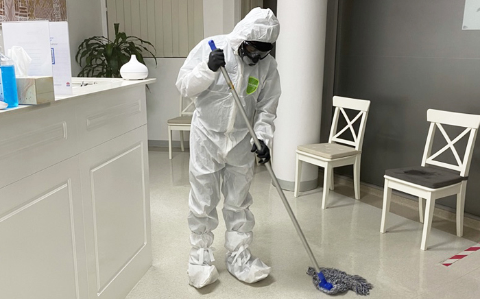 A professional cleaner sanitising office desks in Sydney with gloves and eco-friendly spray.